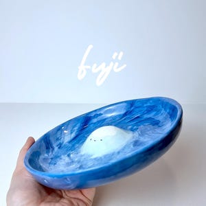 May include: A blue and white ceramic dish with a small white cloud-shaped sculpture inside. The dish has a marbled design and the text "fuji" is written in white above the dish.