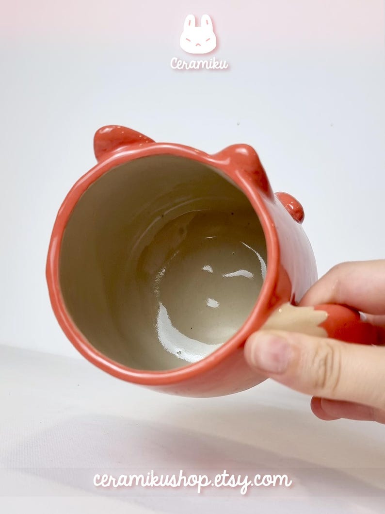 K&ouml;nnte beinhalten: Rote Keramik-Tasse in Fuchsform, mit Ohren und einem Schwanz als Griff. Das Innere ist hellbeige. Auf der Tasse steht "Ceramiku" und "ceramikushop.etsy.com".