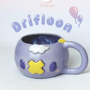 Könnte beinhalten: Helllila Keramikbecher mit Cartoon-Design, einschließlich gelbem Kreuz, weißer Wolke und lila Details. Der Becher hat eine abgerundete Form, einen Henkel und das Wort "Drifloon" in Lila.