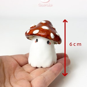 Puede incluir: Figura de cerámica con forma de hongo, de aproximadamente 6 cm de altura, con un sombrero marrón salpicado de puntos blancos. La figura tiene un cuerpo blanco y pequeños ojos negros. Se ve la marca "Ceramiku".