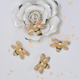 May include: Four gold bee brooches with yellow and black stripes and clear rhinestones. The bees are on a white background.