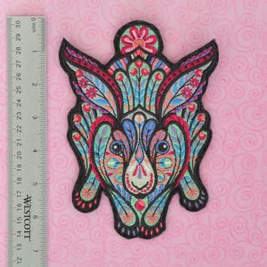 May include: A colorful embroidered patch of a rabbit with a floral design. The rabbit is green, blue, pink, and red with black outlines. The patch is approximately 3 inches in diameter.