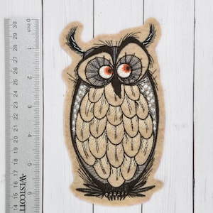 May include: Embroidered felt owl patch with brown, gray, and white details. The owl has large, round eyes with orange pupils. The patch is approximately 3 inches tall.