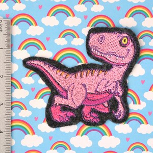 Peut inclure: Patch brodé de dinosaure rose avec un dos en feutre gris. Le dinosaure est en position de course, la gueule ouverte et un œil jaune.