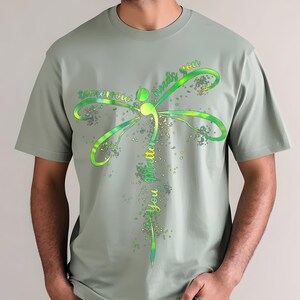 May include: A sage green t-shirt with a green and yellow dragonfly design. The dragonfly has the words "tomorrow needs you" written on its wings and "you matter" written on its body.