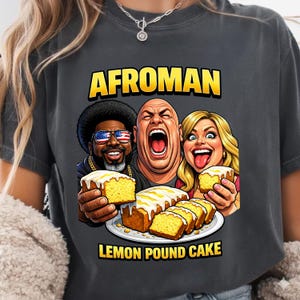 以下が含まれることがあります： レモンパウンドケーキを持った3人の漫画のイラストが描かれた濃いグレーのTシャツ。「AFROMAN」の文字が画像の上に黄色で、下に「LEMON POUND CAKE」と書かれています。