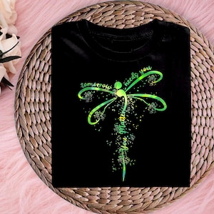 May include: Black t-shirt with a green and yellow dragonfly design. The dragonfly has a semicolon in its body and the text "tomorrow needs you you matter" is written around it.