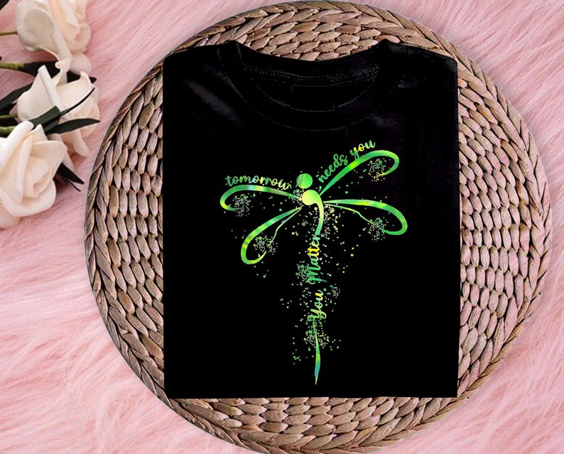 May include: Black t-shirt with a green and yellow dragonfly design. The dragonfly has a semicolon in its body and the text "tomorrow needs you you matter" is written around it.