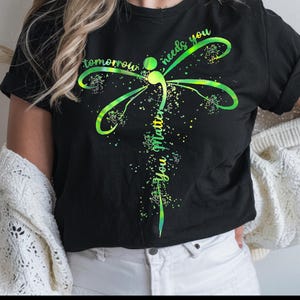 May include: Black t-shirt with a green and yellow dragonfly design. The dragonfly has a semicolon in its body and the text "tomorrow needs you you matter" is written around it.