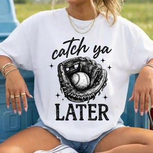 May include: White t-shirt featuring a baseball glove with a baseball inside and the words "catch ya later" in black script. The design includes four small star shapes.
