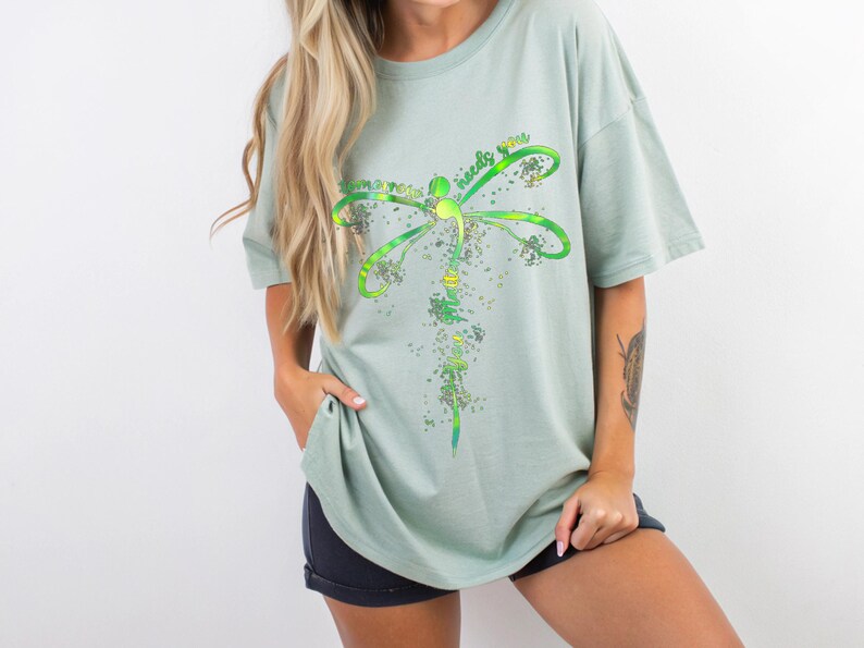 May include: A light green t-shirt with a dragonfly graphic and the text "Sometimes the world needs you".