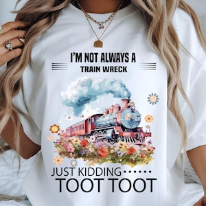 May include: White t-shirt with a colourful train graphic. The design features a vintage steam engine with blue smoke, surrounded by flowers. Text reads "I'M NOT ALWAYS A TRAIN WRECK JUST KIDDING.....TOOT TOOT."