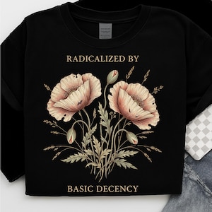 Könnte beinhalten: Schwarzes Sweatshirt mit floralem Design. Es zeigt zwei große, hellpfirsichfarbene Mohnblumen und grüne Blätter. Der Text lautet "RADICALIZED BY" über den Blumen und "BASIC DECENCY" darunter.