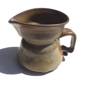 May include: A brown ceramic pitcher with a wide, rounded spout and a handle. The pitcher has a mottled glaze with shades of brown, tan, and white.