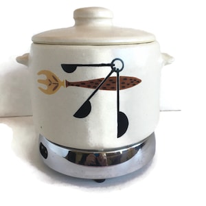 May include: White ceramic slow cooker with a chrome base. The cooker has a lid and a design of a fish and kitchen utensils on the side.