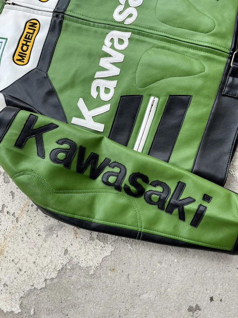 K&ouml;nnte beinhalten: Gr&uuml;ne und schwarze Motorradjacke mit dem Wort "Kawasaki" in wei&szlig;en und schwarzen Buchstaben. Die Jacke hat einen wei&szlig;en und schwarzen Aufn&auml;her mit dem Wort "Michelin". Die Jacke ist aus Leder.