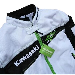 May include: White and black motorcycle jacket with green accents. The jacket has the word "Kawasaki" written on the front in black and white lettering. A green tag with the word "Kawasaki" and the text "Motor Sports Equipment" is attached to the jacket.