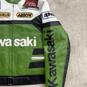 K&ouml;nnte beinhalten: Gr&uuml;ne, wei&szlig;e und schwarze Motorradjacke aus Leder mit "Kawasaki" und "Kawasaki" Text. Die Jacke hat mehrere Aufn&auml;her, darunter "PYROIL THE WINNER" und "ARROW". Die Jacke hat einen Rei&szlig;verschluss und einen Schnallenriemen.