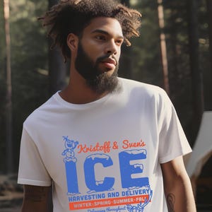 以下が含まれることがあります： クリストフとスヴェンのアイス収穫と配送サービスを特徴とする、青と赤のグラフィックプリントが施された白いTシャツ。グラフィックには雪だるま、トナカイ、そして「Kristoff & Sven's ICE HARVESTING AND DELIVERY WINTER-SPRING-SUMMER-FALL! Delivering throughout Arendelle Kingdom CONTACT SVEN FOR DETAILS.」というテキストが含まれています。