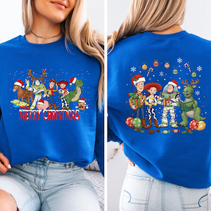 May include: Royal blue sweatshirt featuring a festive design with cartoon characters, including a dinosaur, a spaceman, and a cowboy, all wearing Santa hats. The front of the sweatshirt has the text "MERRY CHRISTMAS".