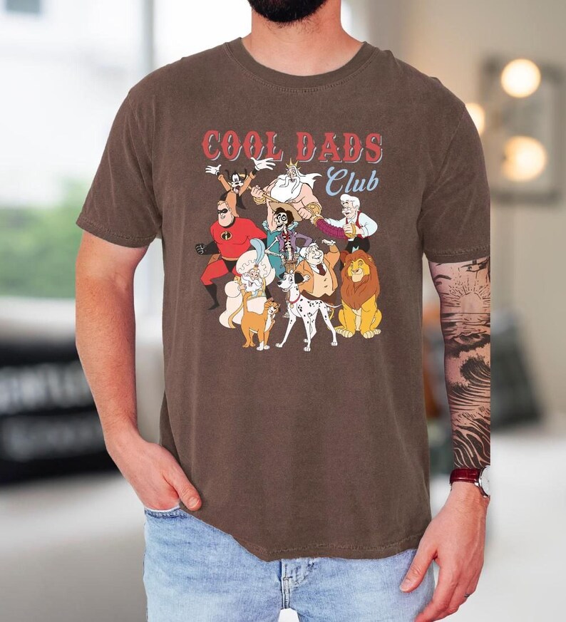 A man wearing a brown t-shirt with a graphic design of cartoon characters from the animated film "Cool Dads Club".