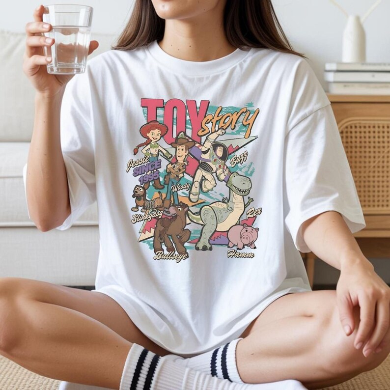 A person wearing a white t-shirt with a colorful graphic of characters from the Toy Story movie, including Woody, Buzz Lightyear, and other beloved characters.