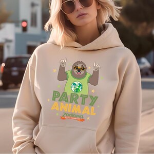 A woman wearing a beige hoodie with a graphic of a cartoon sloth and the text "PARTY ANIMAL ZOO" printed on it.