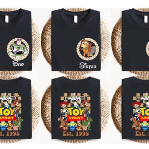 Puede incluir: Camisetas negras con gr&aacute;ficos de Toy Story. Algunas camisetas presentan a Buzz Lightyear, Slinky Dog y Rex. Otras muestran el logo de Toy Story con personajes y el texto "Est. 1995". Las camisetas est&aacute;n sobre un fondo tejido.