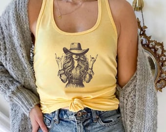 May include: A yellow Banana Cream tank top featuring a graphic of a woman wearing a cowboy hat and making a rock and roll hand gesture. The woman has long, flowing hair and is wearing a belt. The tank top is made of a soft material.