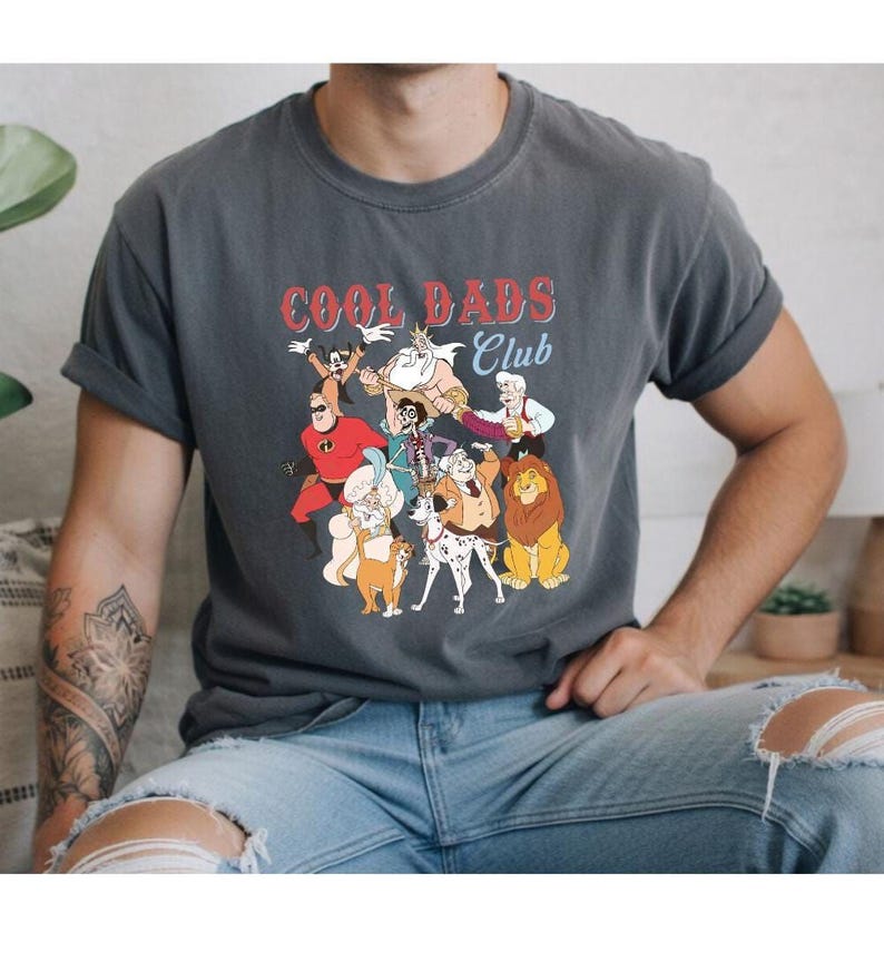 A person wearing a gray t-shirt with a graphic design featuring cartoon characters and the text "Cool Dads Club".