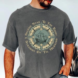 May include: Gray t-shirt featuring a compass design with a sailing ship illustration at the center. The text around the compass reads "Second Star to the Right Straight on 'Til Morning."