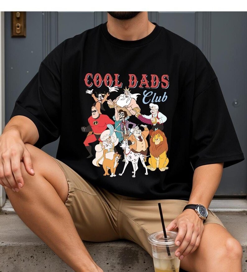 A person wearing a black t-shirt with a graphic of cartoon characters and the text "Cool Dads Club" is sitting on a step.