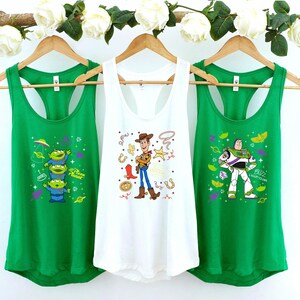 Three green tank tops hanging on a rack, each with a different cartoon character design.
