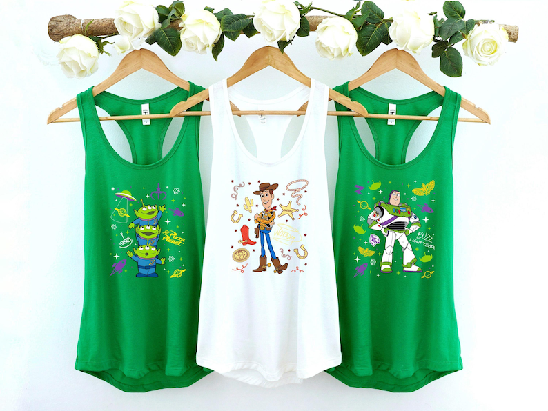 Three green tank tops hanging on a rack, each with a different cartoon character design.