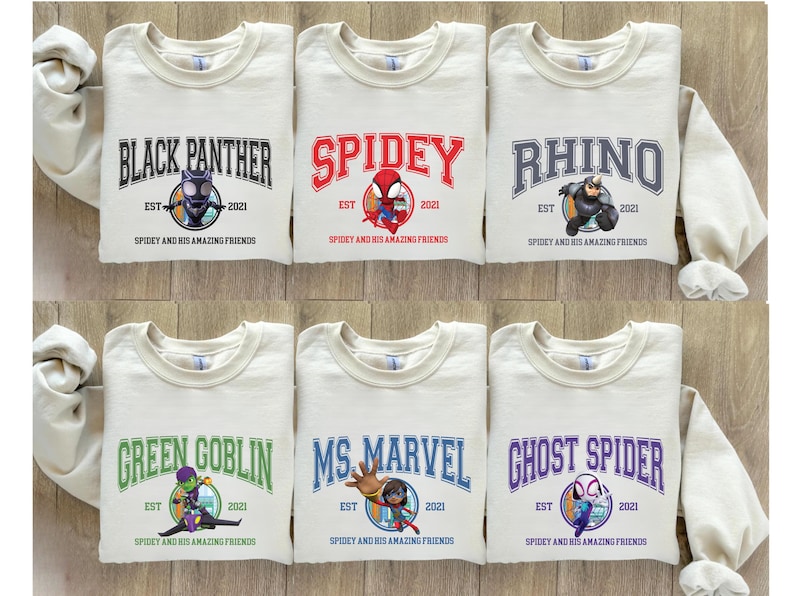 Puede incluir: Seis sudaderas de color crema con diferentes dise&ntilde;os de personajes de superh&eacute;roes. Cada sudadera presenta un personaje del universo Spider-Man, incluyendo Black Panther, Spidey, Rhino, Green Goblin, Ms. Marvel y Ghost Spider. El texto en cada sudadera dice "Spidey and his amazing friends" e incluye el a&ntilde;o "2021".