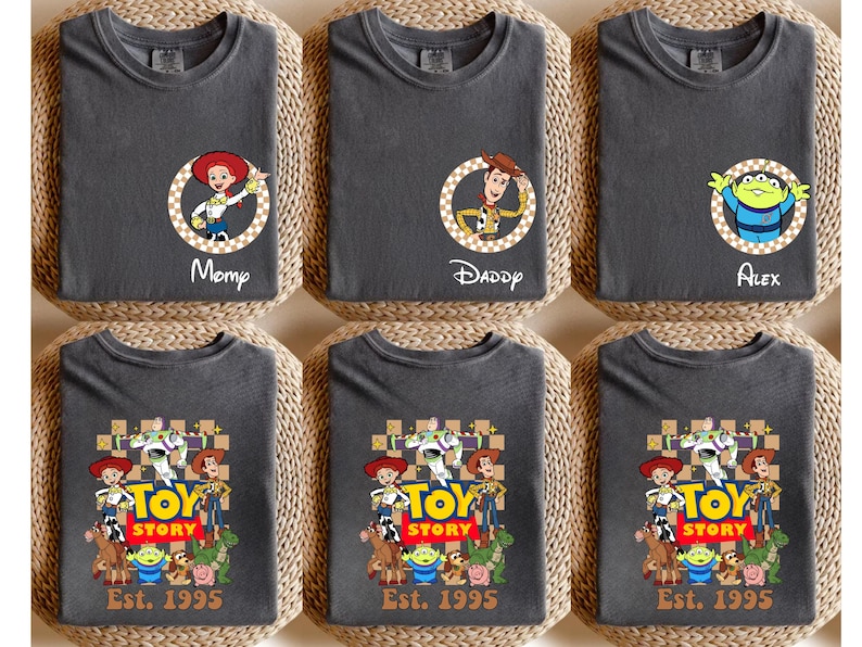 Puede incluir: Camisetas gris oscuro con personajes de Toy Story. Algunas camisetas tienen retratos de personajes con nombres como "Momp", "Daddy" y "Alex". Otras camisetas muestran un grupo de personajes con el texto "TOY STORY Est. 1995".