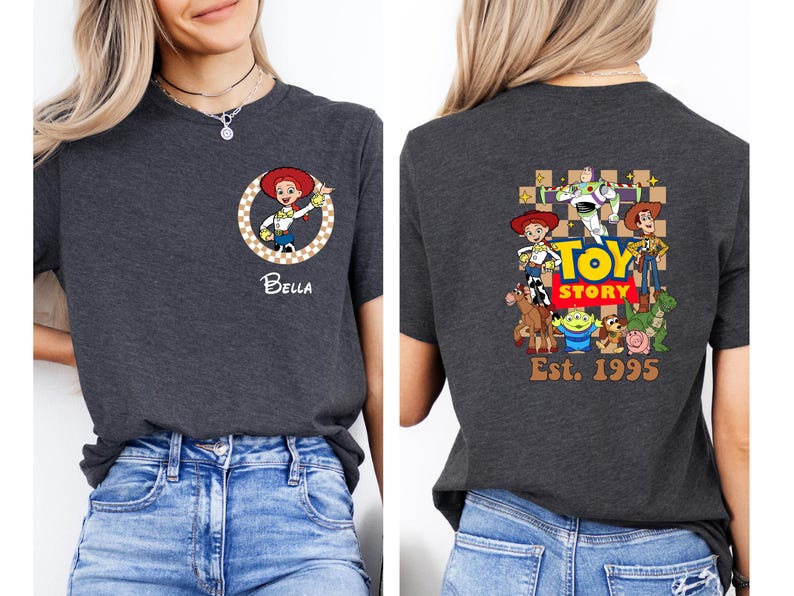 Puede incluir: Camiseta gris oscuro con un gr&aacute;fico del personaje Jessie y el nombre "Bella" en la parte delantera. La parte trasera de la camiseta muestra un gr&aacute;fico de "Toy Story" con personajes y el texto "Est. 1995".