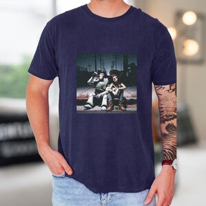 A man wearing a navy blue t-shirt with a graphic design featuring two people sitting on a bench.