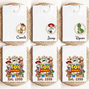 Puede incluir: Camisetas blancas con personajes de Toy Story. Algunas camisetas tienen nombres como "Charlie", "Jenny" y "Dylon". Otras camisetas muestran el logotipo de Toy Story y el texto "Est. 1995".
