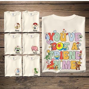 May include: Off-white t-shirts with various Toy Story character designs and the text "Name". A larger shirt features the phrase "YOU'VE GOT A FRIEND IN ME" in colorful letters with character illustrations.