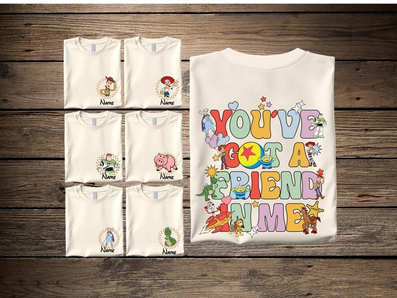 A collection of white t-shirts with various cartoon characters and a large t-shirt with a colorful message printed on it, all laid out on a wooden surface.