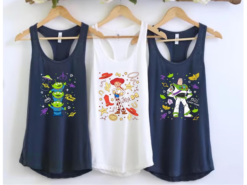 Three shirts hanging on a rack, each featuring a different character from the Toy Story franchise.