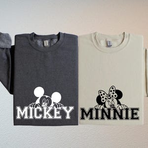 two t-shirts with the word "MICKEY" and the word "MINNIE" printed on them, along with the iconic Mickey Mouse and Minnie Mouse logos.