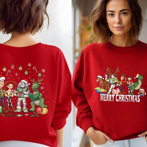 May include: Red sweatshirt featuring a graphic of Toy Story characters in Santa hats with the text "MERRY CHRISTMAS". The design includes Woody, Buzz Lightyear, and Rex. Festive holiday apparel.