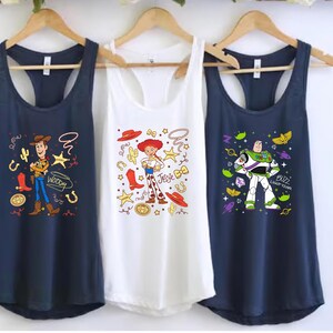 Three t-shirts hanging on a rack, each featuring a different character from the Toy Story franchise.