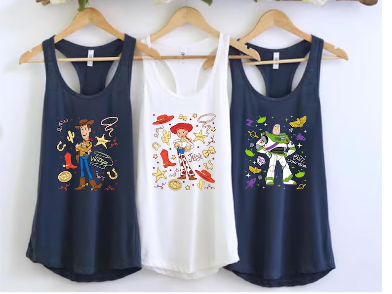 Three t-shirts hanging on a rack, each featuring a different character from the Toy Story franchise.
