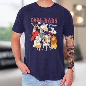 A man wearing a navy blue t-shirt with a graphic design featuring cartoon characters and the text "Cool Dads Club".