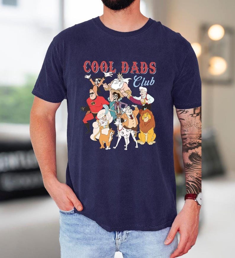 A man wearing a navy blue t-shirt with a graphic design featuring cartoon characters and the text "Cool Dads Club".