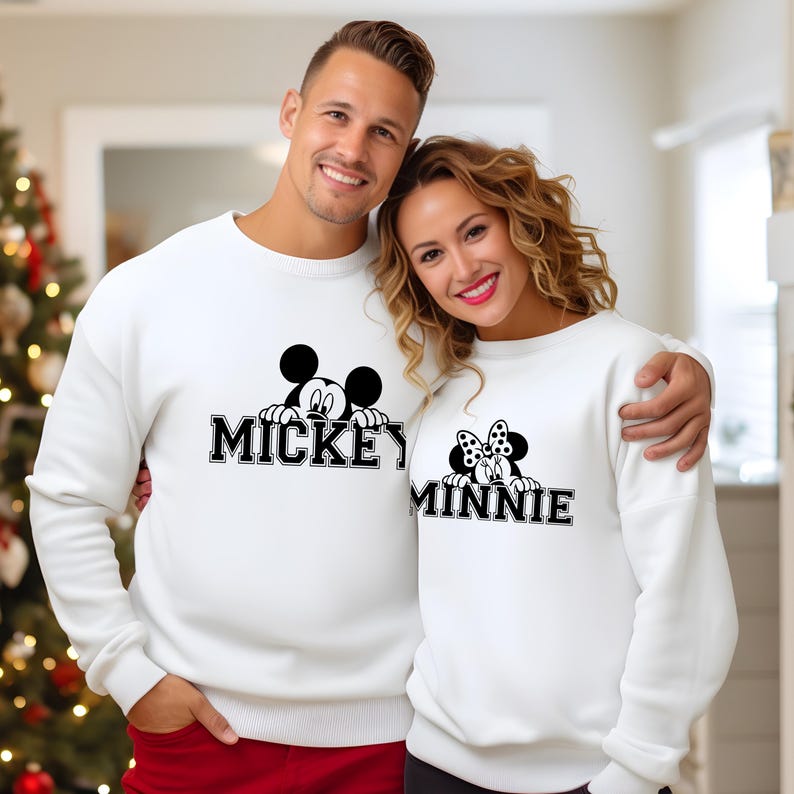 A man and a woman are standing close together, both wearing white sweaters with the Mickey Mouse logo.