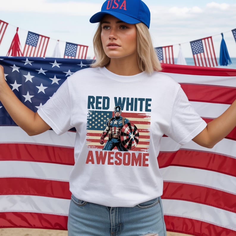 May include: A white short-sleeve t-shirt featuring a graphic of Captain America holding a shield in front of an American flag. The text "RED WHITE" appears in blue above the character, and "AWESOME" in red below, with a distressed vintage effect.